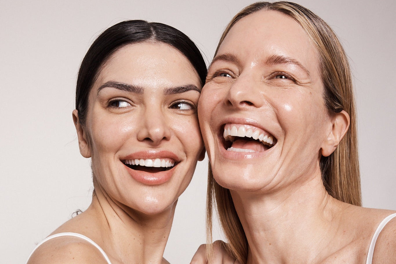 Two women with glowing, hydrated skin laughing together after Hydrafacial treatments.