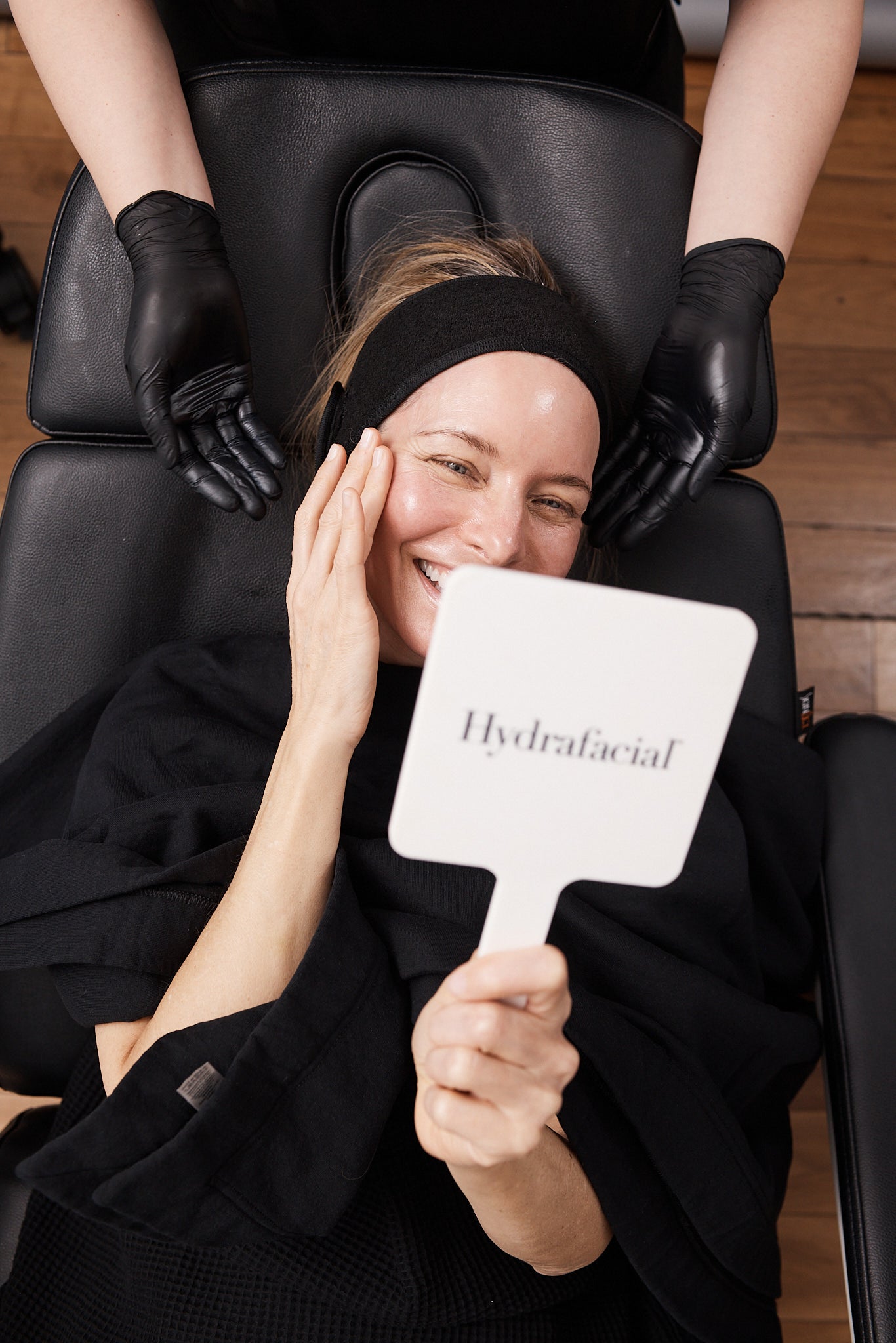 Smiling client holding a Hydrafacial mirror while admiring her results after treatment.