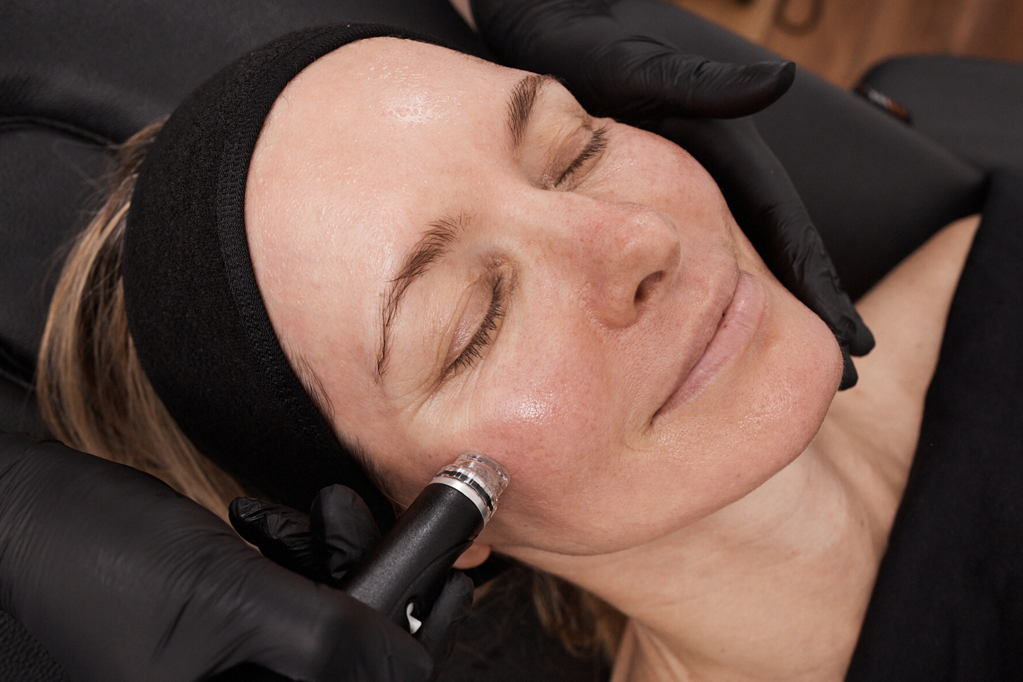 Client reclines with eyes closed as a Hydrafacial device is applied to the cheek, leaving the skin hydrated and luminous.