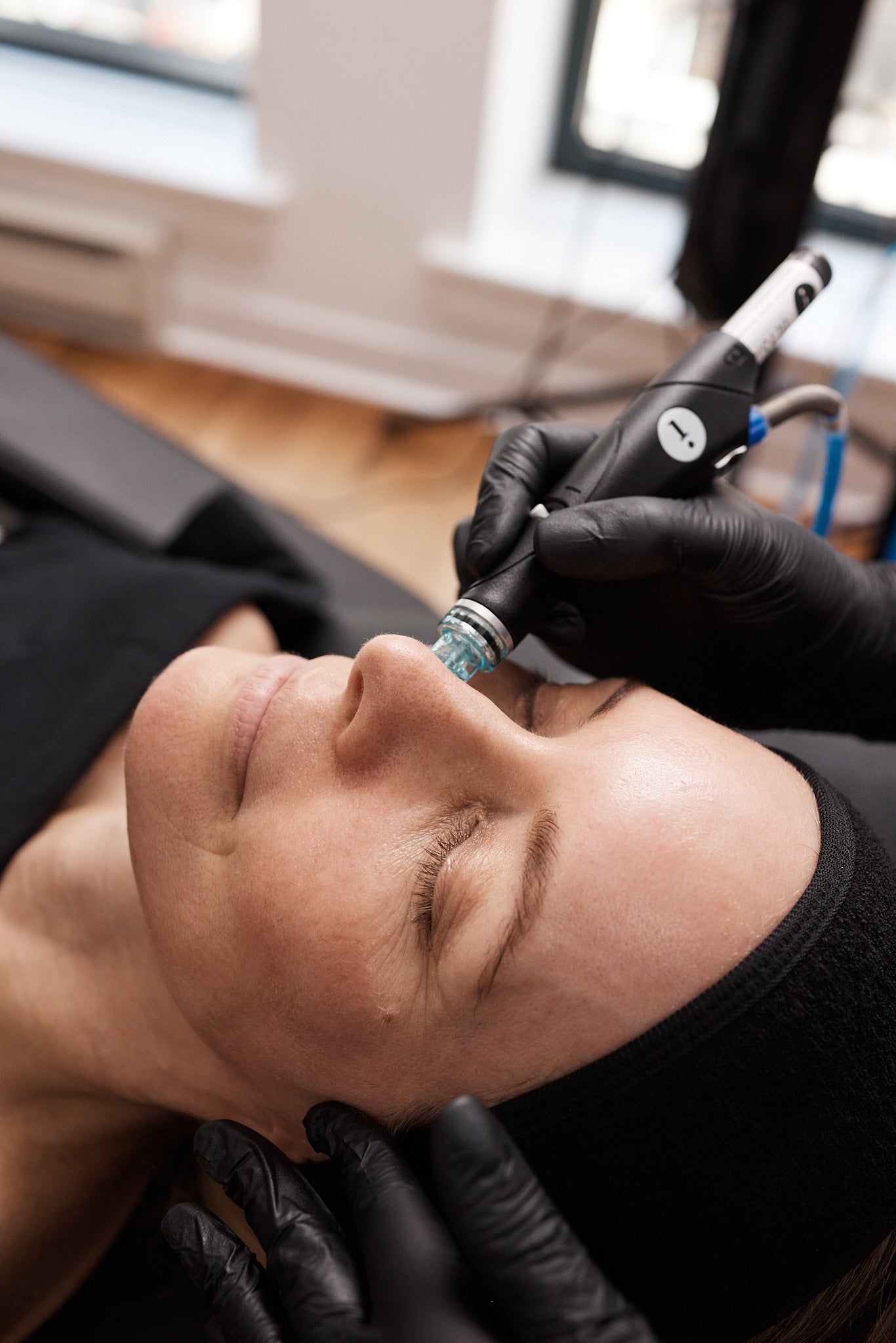 Close-up of a Hydrafacial device applied to a client’s nose. Both the suction tip and the esthetician’s gloved hands are visible during extraction.