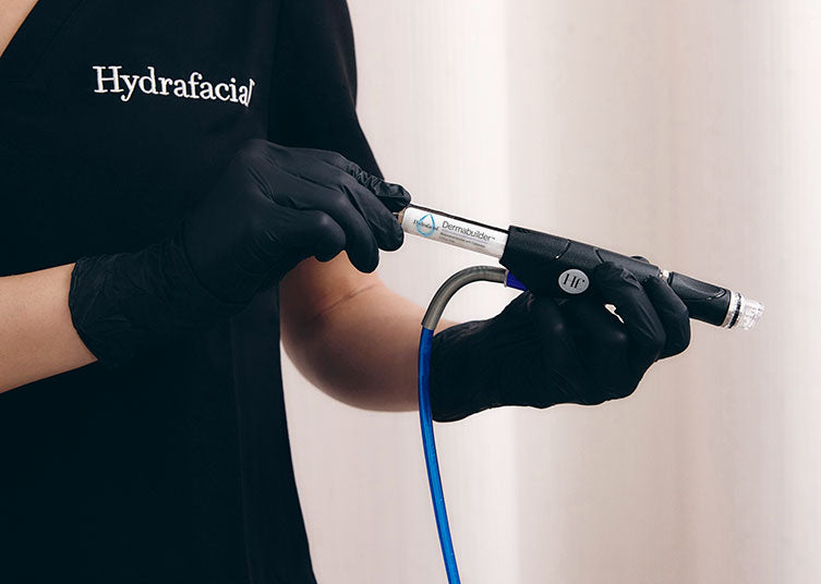 Hydrafacial provider wearing black gloves holding the treatment wand with a booster vial attached.