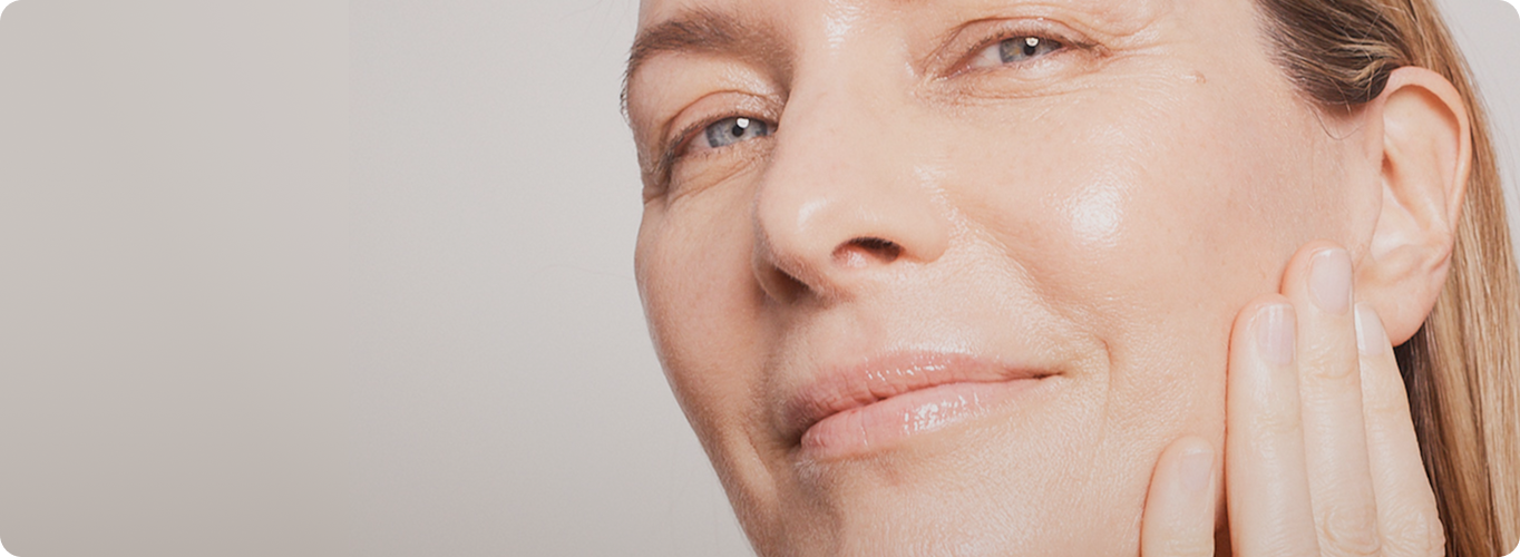 A close-up view of a woman with glowing skin gently touching her cheek, smiling confidently after treatment.