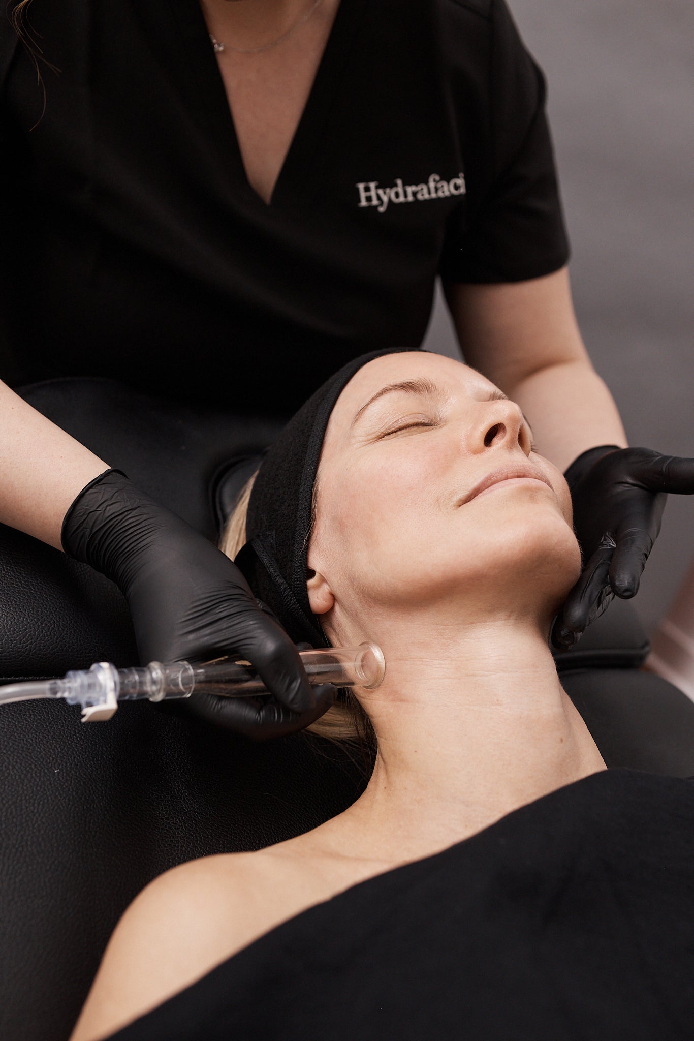 A gloved hand holds a device with a blue tip against the cheekbone near the nose of a person lying back with eyes closed.