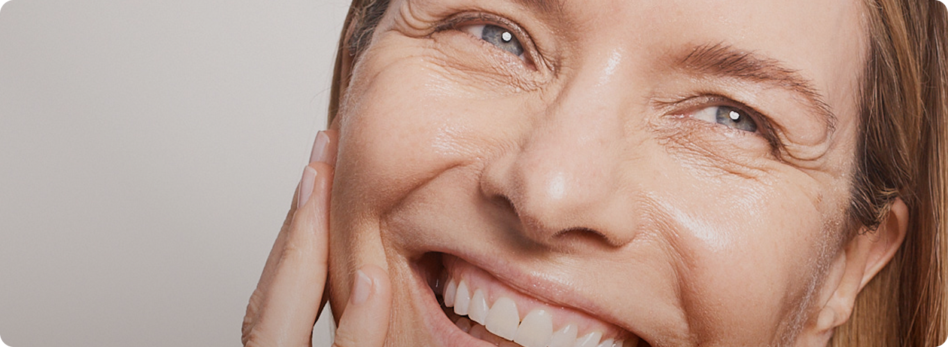 Close-up of a woman laughing with eyes closed, her skin appearing luminous and hydrated.